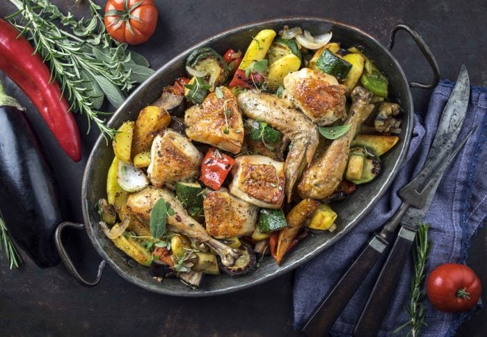 Chicken pieces roasting in pan with vegetables