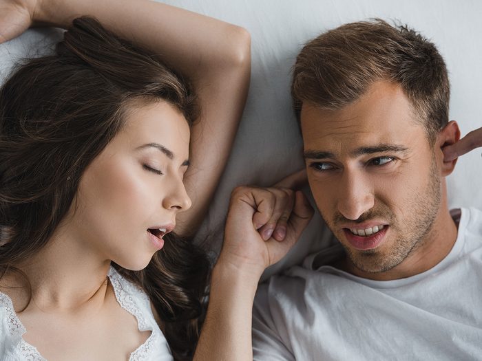 Woman snoring in bed while man plugs ears