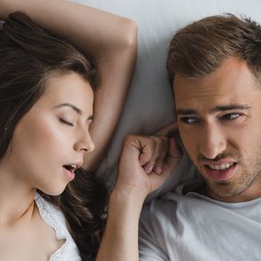 Woman snoring in bed while man plugs ears