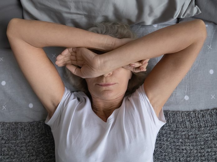 Top view aged woman lying on bed woke up at night due noisy neighbors. Mature female cover face with hands suffers from insomnia sleep disorder, has restless obsessive thoughts keep her awake concept