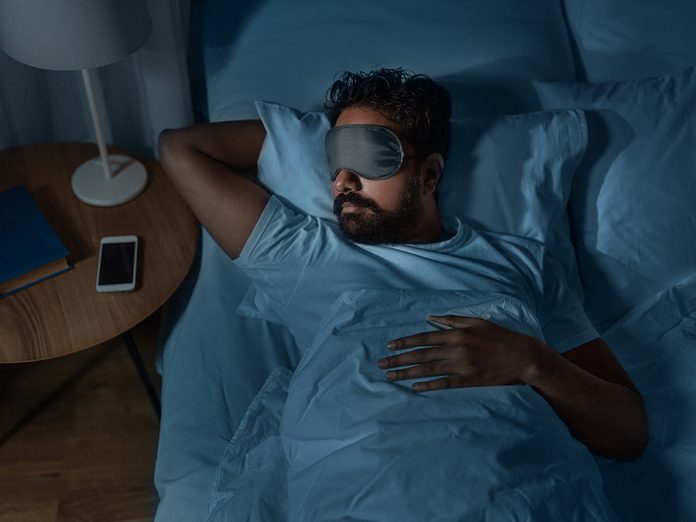 people, bedtime and rest concept - indian man in eye mask sleeping in bed at home at night