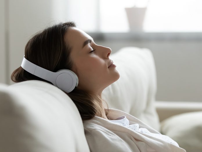 Peaceful girl in modern wireless headphones sit relax on comfortable couch listening to music, happy calm young woman in earphones rest on cozy sofa, enjoy good quality sound, stress free concept