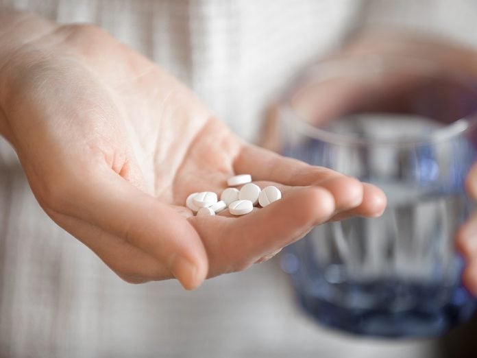 Healthcare, treatment, supplements. Handful of white round pills in female patients palm, woman arm holding heap of small round meds and glass of water, shallow depth of field, focus on medicine