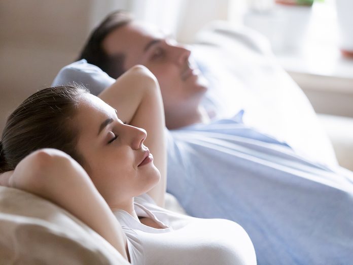 Close up of mindful husband and wife sleeping on sofa relaxing hands over head, calm man and woman lying on cozy couch taking nap at home, millennial couple enjoying rest with eyes closed dreaming