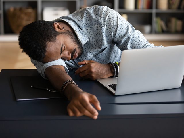 Exhausted tired African American businessman entrepreneur lying on desk with closed eyes, falling asleep, overworked young man unmotivated student sleeping at workplace, boring routine work