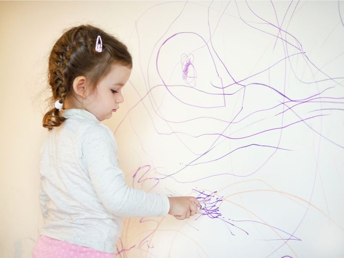 Little girl drawing on wall with crayon