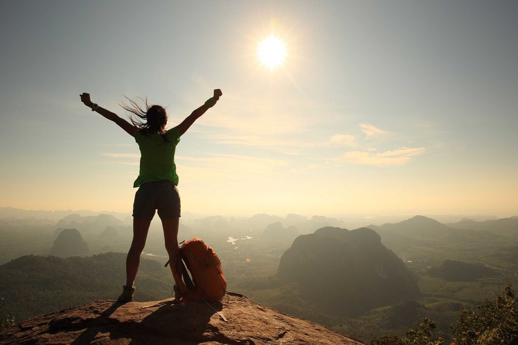 Confidence lessons - Confident woman cheering on mountain peak