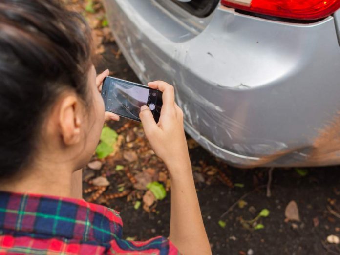 Young woman photographing damage on car