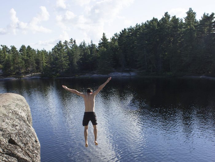 Photo by Noorbanu Mohamedali of man jumping off cliff into lake