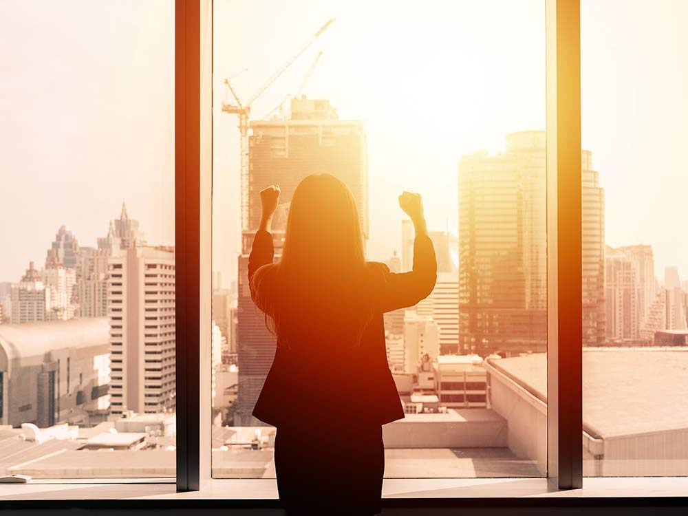 Businesswoman with arms up by office window
