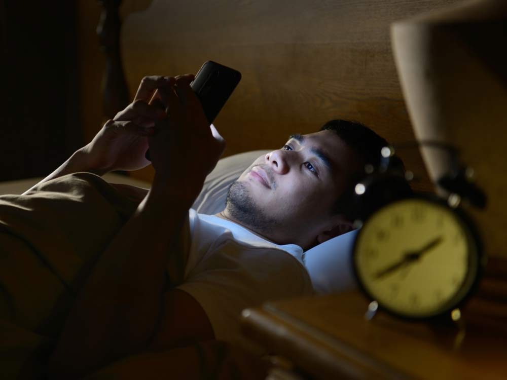 Man browsing through smartphone in bed at night