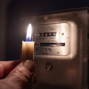 A man's hand with candle in complete darkness looking on electricity meter at home. Power outage, blackout concept.