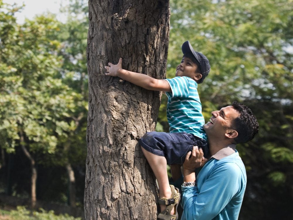 Father helping young son climb tree