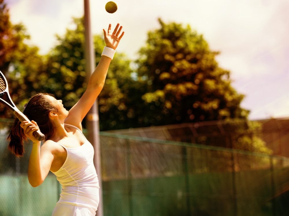 Woman playing tennis and throwing tennis ball