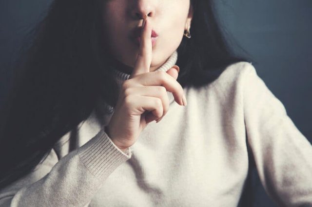 close up of young woman holding finger on lips