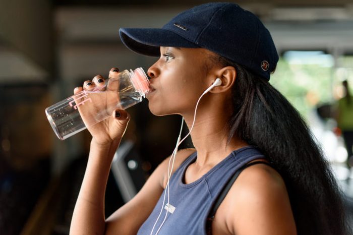 Close-up of black gorgeous woman fitness instructor drinking water during the training exercises in gym
