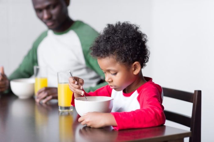 happy african-american father and little son eating breakfast