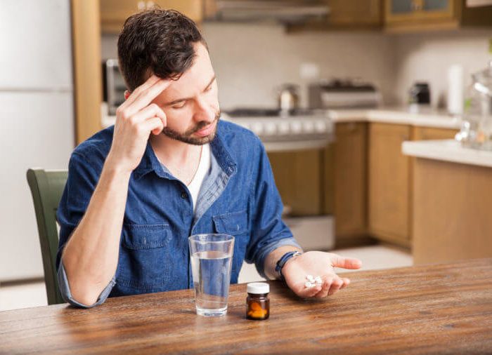 Young hungover man taking some pills to cure a headache at home