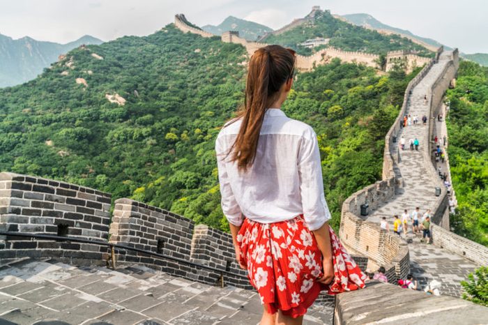 Young girl tourist from behind looking at view of Great Wall of China at famous Badaling tourism attraction during travel vacation in Beijing. Asia summer holidays.