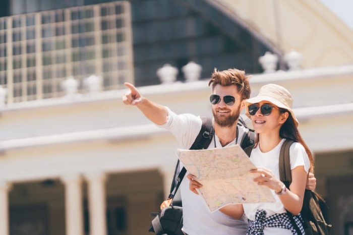 Multiethnic traveler couple using generic local map together on sunny day, man pointing toward copy space. Honeymoon trip, backpacker tourist, Asia tourism, or holiday vacation travel concept.