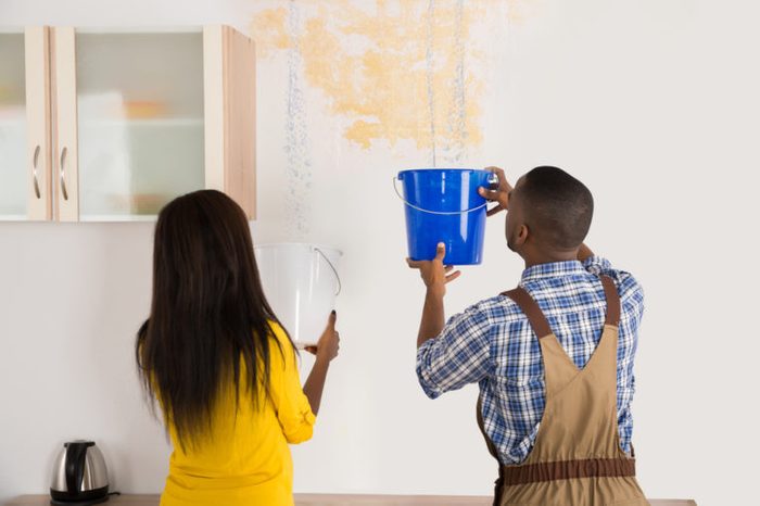 Young African Woman Standing With Worker Collecting Water In Bucket From Ceiling In House