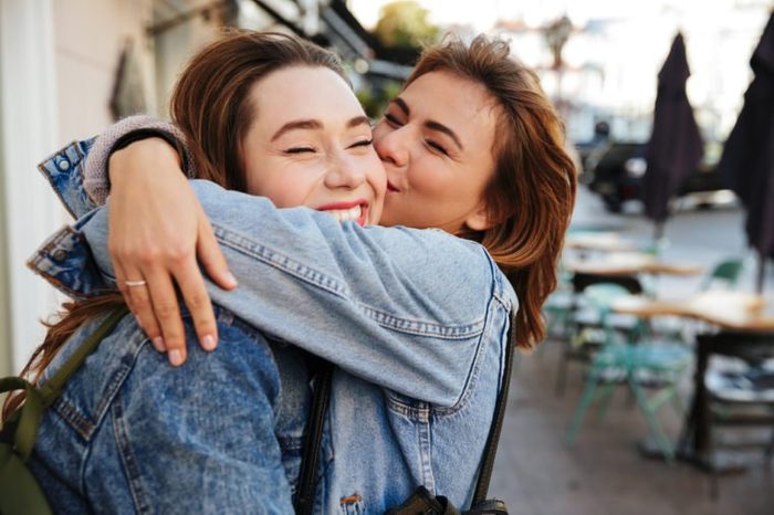 Close-up photo of two emotional happy woman friends hugging each other on city street