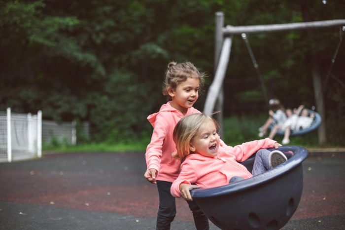 Two cute little girls playing in the playground outside in park. Summer, fun, family and vacations concept. Two sisters having fun.