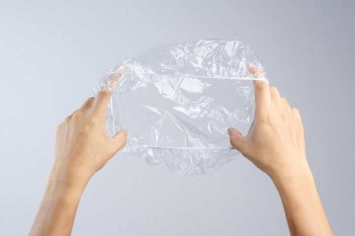 Hand holding disposable transparent plastic shower cap on white background