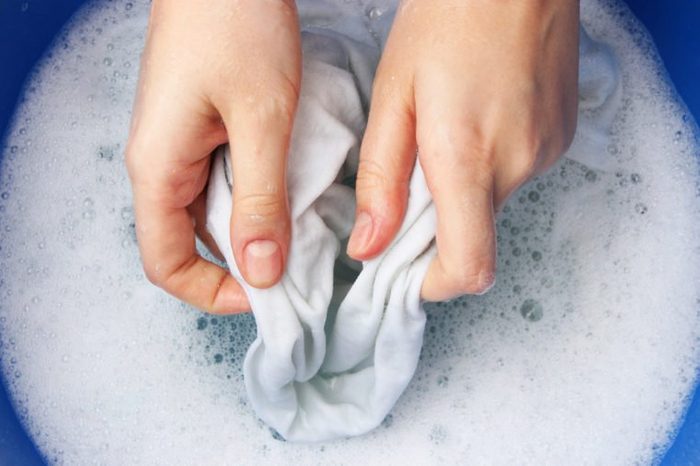 A woman washes clothes by hand in soapy water.