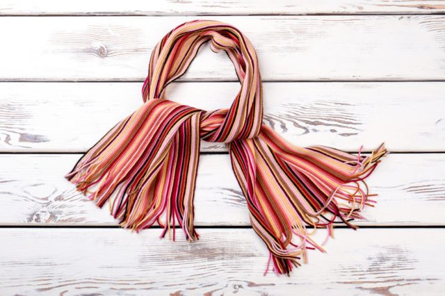 Multicolored striped scarf, wooden background. Colorful knitted scarf for women.