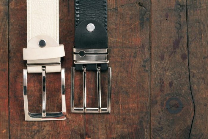 White and black leather belts hanging on old wooden background