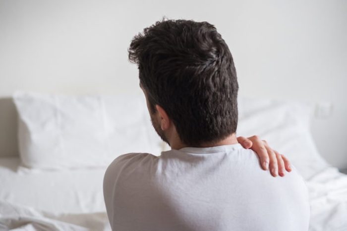Rear view of one man sitting on bed having back pain
