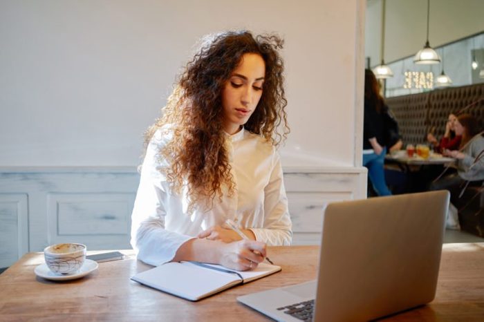 Young attractive business woman holds a job interview in a cafe during the lunch break. businesswoman searching for information on the Internet and makes notes in a notebook
