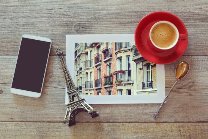 Photo of buildings in Paris on wooden table with coffee cup and smart phone. View from above