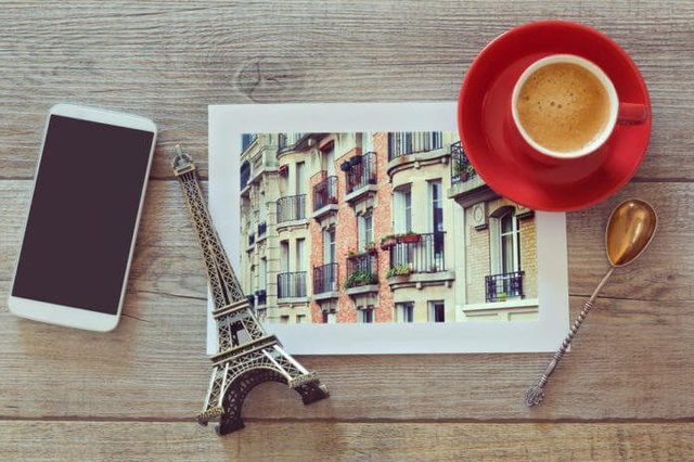 Photo of buildings in Paris on wooden table with coffee cup and smart phone. View from above