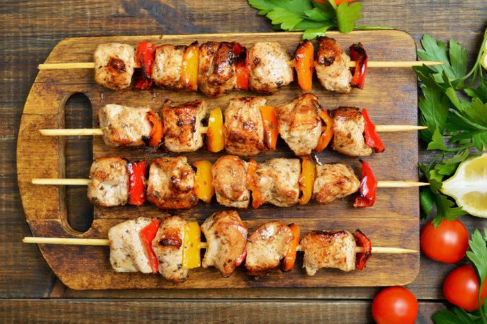 Grilled chicken kebabs on wooden cutting board, top view