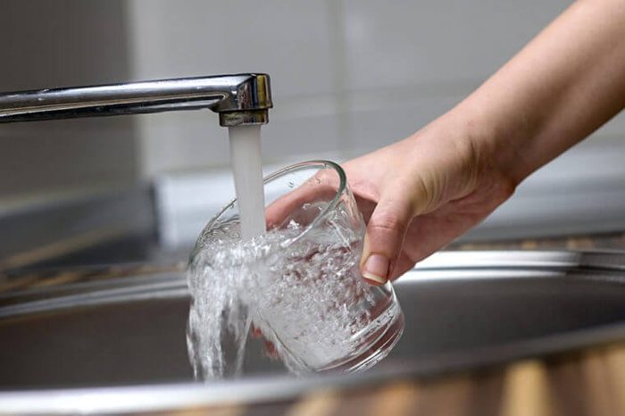 Female hands pouring water in glass cup from a kitchen faucet. Woman hand's filling the glass of water. Filling glass of water from stainless steel kitchen faucet