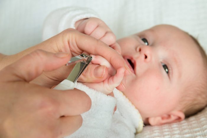 Mother cutting baby's fingernails with nail clippers.