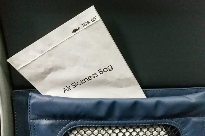 Air sickness bag tucked behind airplane seat pocket for nauseous passenger