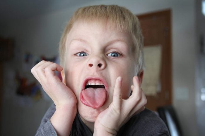 A six year old boy child is being funny and making a bratty face while sticking out his tongue.