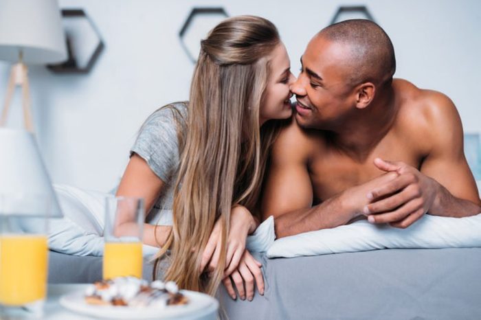 multicultural couple kissing and lying on bed