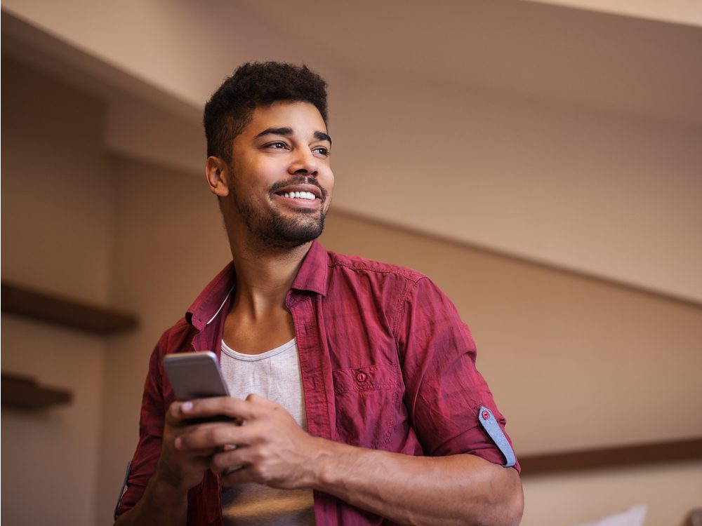 Man smiling while messaging friend on his smartphone