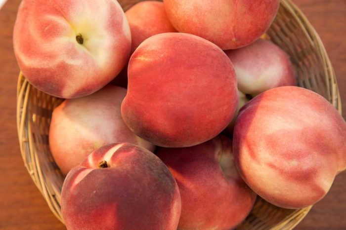 Some peaches in a basket over a wooden surface seen from above