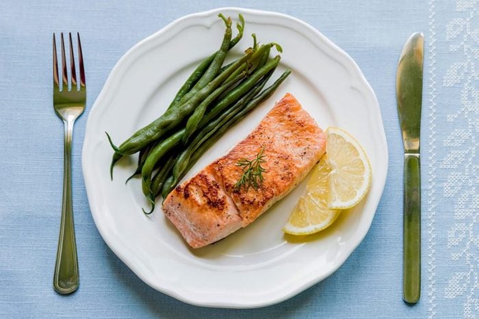 Grilled salmon fillet with green beans and lemon on white plate from above