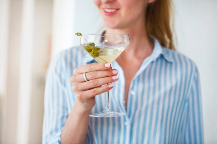 Woman holding glass with martini and green olives, focus on olives 