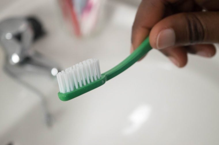 Cropped image of dark skin fingers holding toothbrush in bathroom sink Dental care. African American Woman hands is holding toothbrush in bathroom sink faucet in background