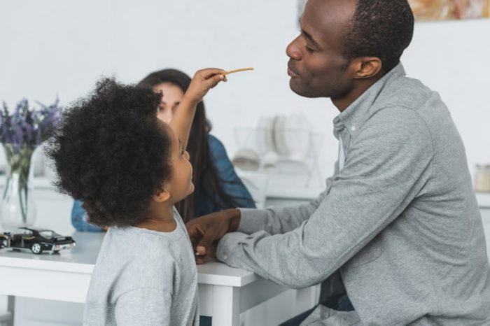 african american son feeding father with crispy breadsticks at home