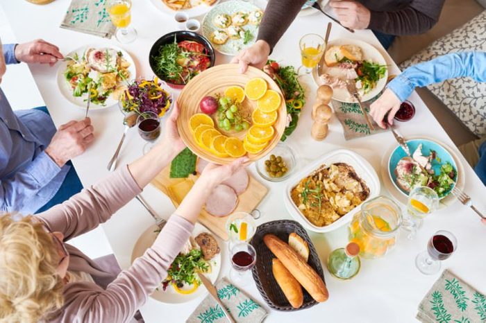 Top view of big happy family sitting at dinner table enjoying delicious homemade food during festive celebration and handing fruit plate across table
