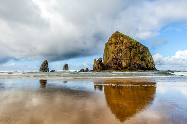 Oregon coast scenic Haystack Rock on a dramatic day with clouds and reflections. Famous destination for bird watchers.
