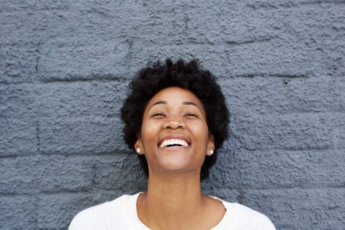 Closeup portrait of beautiful african young woman laughing against grey wall